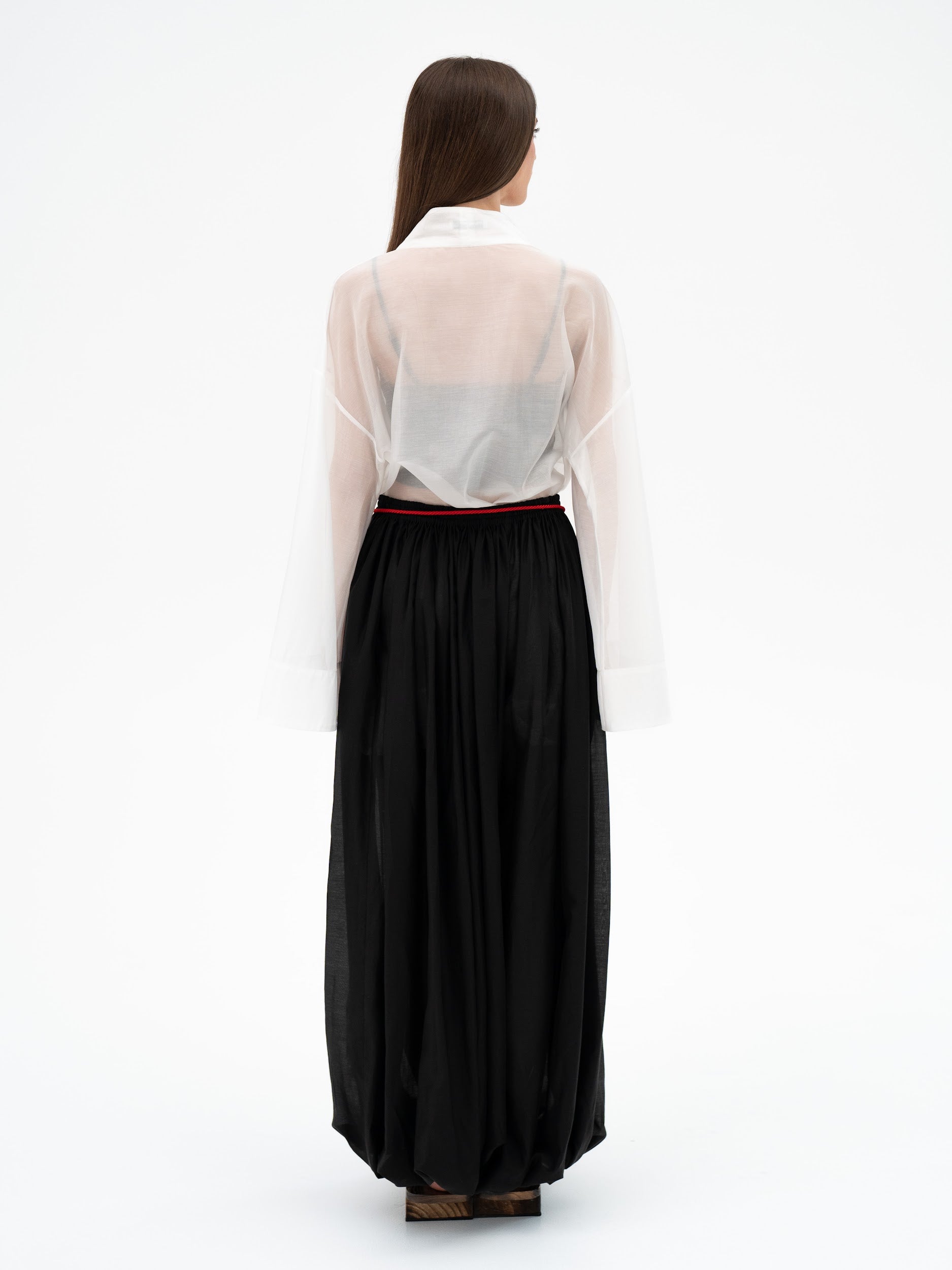 Woman wearing a long black trousers and sheer white blouse on a white background