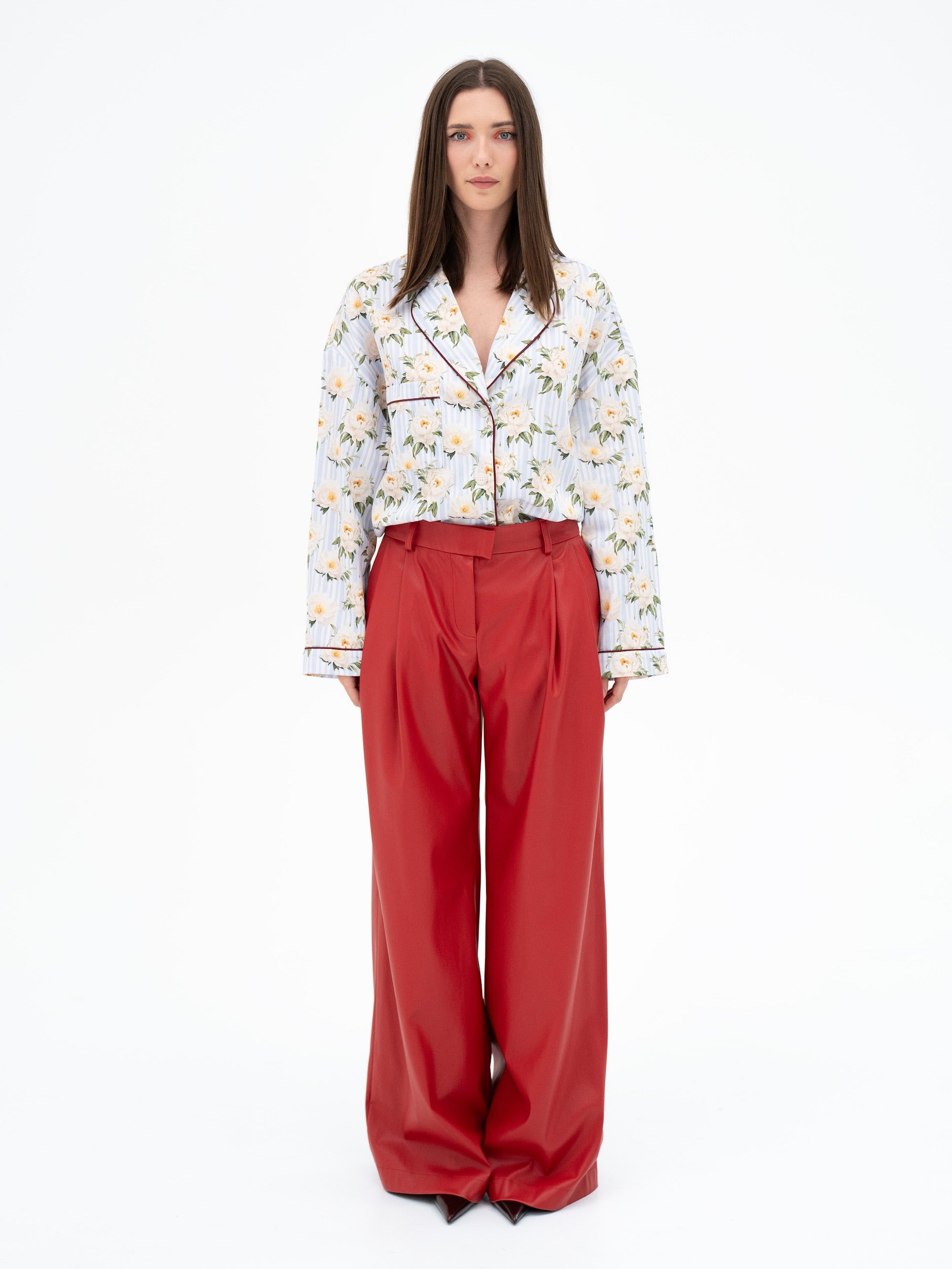 Woman wearing a floral blouse and red pants on a white background