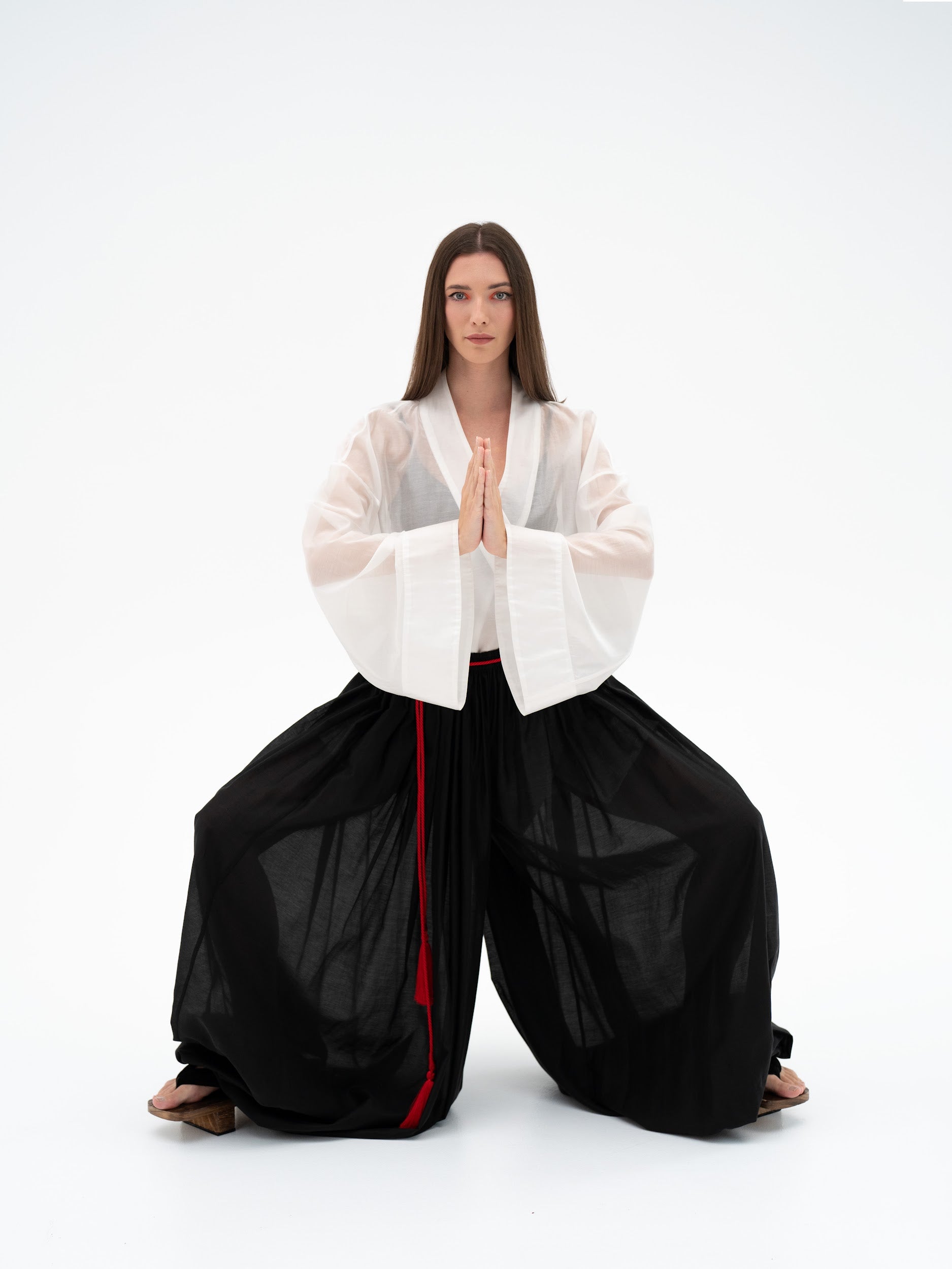 Person wearing a white top and black pants with a red stripe on a white background