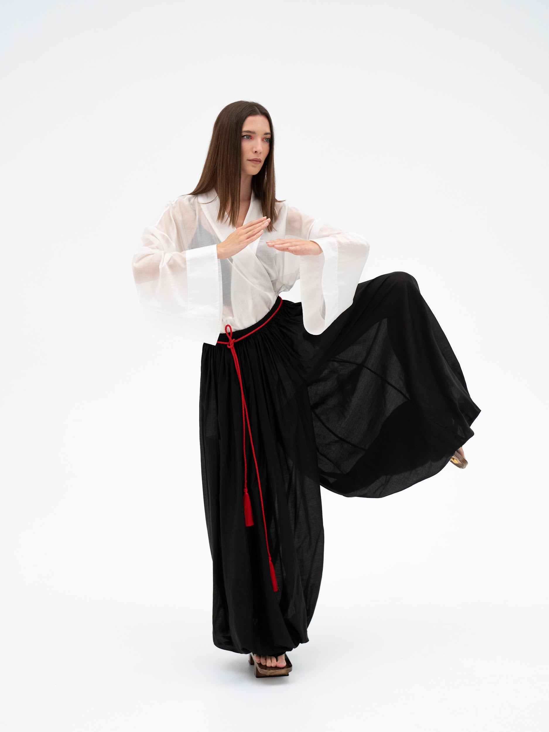 Woman in a white blouse and black ballon pants with red accents on a white background
